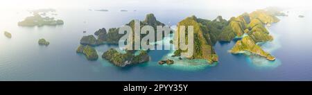 Korallenriffe umgeben die zerklüfteten Kalksteininseln, die sich aus der Meereslandschaft von Raja Ampat erheben. Dieser abgelegene Teil Indonesiens weist eine hohe biologische Vielfalt der Meere auf. Stockfoto