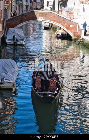 Blick auf einen Gondoliere von der Rückseite einer Gondel in einem engen Kanal in Venedig Stockfoto