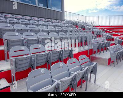 Reihen mit leeren grauen Sitzen in einem Stadion mit silbernen Zahlenschildern in Form von Baseballs oder Softballs. Stockfoto