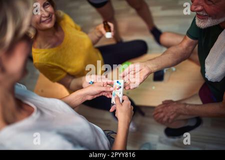 Seniorin und Seniorin in Umkleidekabinen unter Einnahme von Medikamenten und Vitaminen von jungen Frauen. Vorbereitung auf das Fitnesstraining. Das Seniorenlebenskonzept. Stockfoto