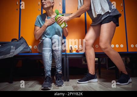 Junge sportliche Frau hilft Seniorin mit Übelkeit in der Sporthalle, fühlt sich krank vom Training. Das Seniorenlebenskonzept. Stockfoto