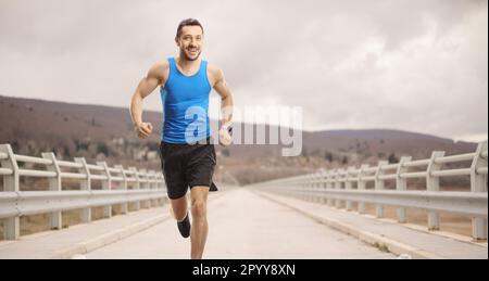 Fit Mann in Sportbekleidung, der an einem bewölkten Tag über eine Brücke läuft Stockfoto