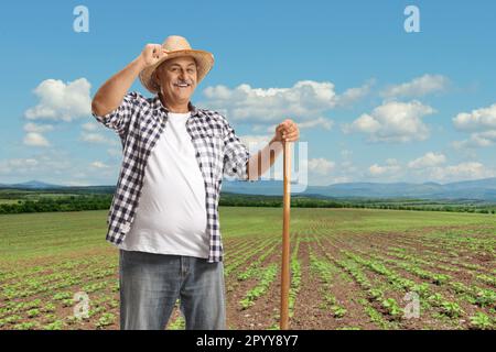 Lächelnder reifer Bauer, der auf einem Feld posiert und mit seinem Strohhut begrüßt wird Stockfoto