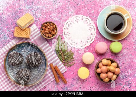 Top View leckere Schokoladenkuchen mit einer Tasse Tee und Makronen auf einem rosafarbenen Kuchen Kekskuchen Kuchen süßer Puderzucker Stockfoto