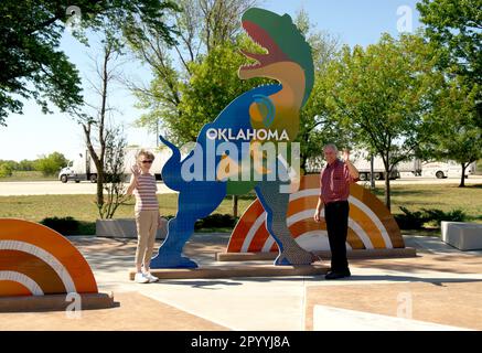 Das Seniorenpaar im Oklahoma Welcome Center, USA, steht neben dem farbenfrohen Dinosaurier vor der Kamera. Stockfoto