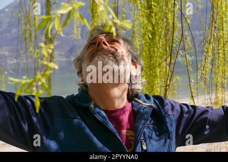 Ein Mann mit einem inhaltlichen Ausdruck steht in einer üppigen grünen Umgebung, mit ausgestreckten Armen Stockfoto