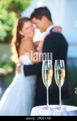 Zeit zum Feiern. Glückliche junge Vermählte mit Schwerpunkt auf Gläsern Champagner im Vordergrund. Stockfoto