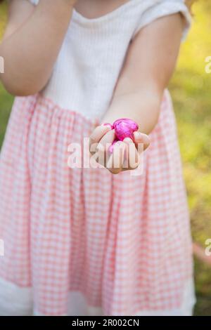 Ein kleines Mädchen mit einer Faust voller rosa ostereier, die bei der Jagd gefunden wurden Stockfoto