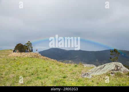 Farbenfroher Regenbogen an einem bedeckten Tag über Hügel und Tal im Hunter Valley in St. Clair mit weit entfernten Menschen Buschwanderungen Stockfoto