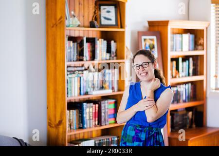 Porträt einer lächelnden jungen Frau in ihrem Haus mit Bücherregalen an Wänden voller fiktiver Geschichten Stockfoto