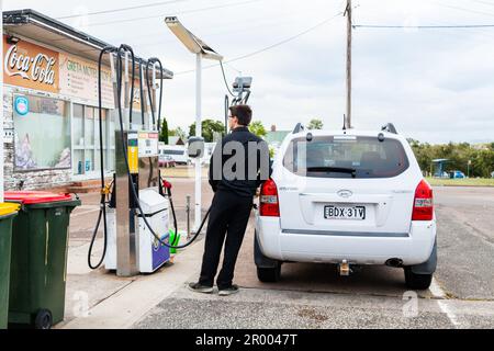 Ein junger Mann in Schwarz betankt sein Auto an einer ländlichen Tankstelle in einer australischen Landstadt Stockfoto