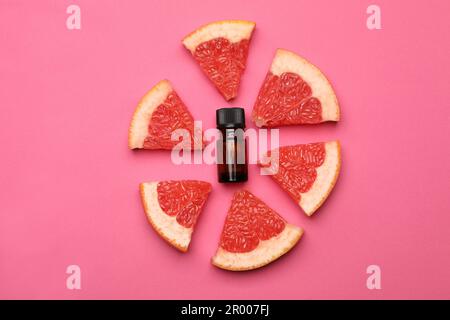 Flasche ätherisches Zitrusöl und frische Grapefruitscheiben auf pinkfarbenem Hintergrund, flach liegend Stockfoto