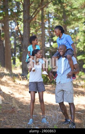 Ich gebe den Kindern eine Pause von der Wanderung. Porträt einer Mutter und eines Vaters, die ihre Kinder auf den Schultern tragen, während sie wandern. Stockfoto