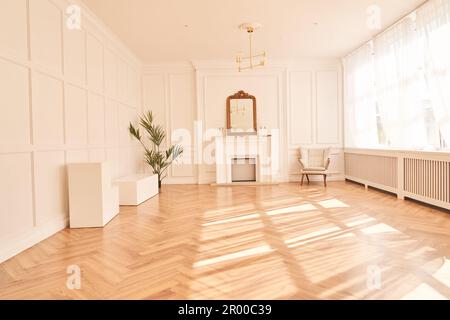 Helle Einrichtung mit großen Fenstern und einem Kamin im klassischen Stil. Großes Wohnzimmer mit Dekorartikeln. Wunderschönes Parkett und Kopierraum. Sonnenlicht und Schatten im Raum. Hochwertiges Foto Stockfoto