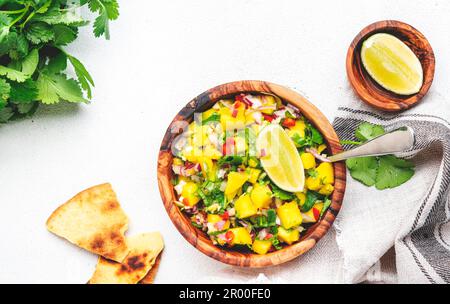 Mango Salsa – scharfe Sauce mit Chili-Paprika, Zwiebeln, Knoblauch, Limette und Koriander in einer Holzschüssel auf weißem Tischhintergrund, Draufsicht Stockfoto