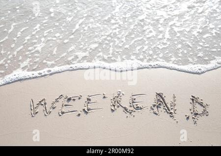 Das Wort "WOCHENENDE" wurde von Hand in den Sand geschrieben. Nahaufnahme der Sandtextur am Strand im Sommer. Urlaub, Urlaubskonzept, Stockfoto