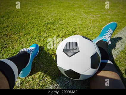 Sport, Spielfeld und Schuhe eines Mannes mit Fußball im Freien, entspannen und ausruhen nach Fitness oder Training. Fußball, Pov und männlicher Spieler entspannen sich auf dem Gras Stockfoto