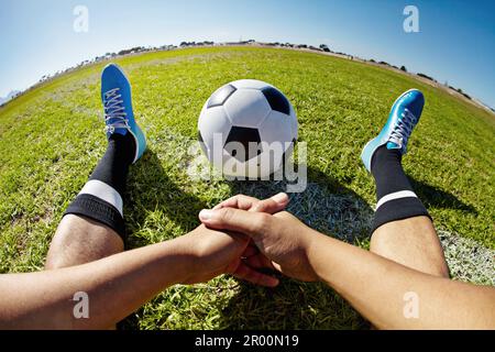 Sport, Pov und Schuhe von Mann mit Fußball im Freien, entspannen und ausruhen nach Fitness oder Training. Fußball, Spielfeld und männlicher Spieler entspannen sich auf dem Gras Stockfoto