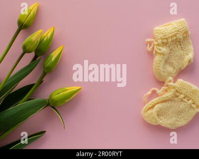 Tulpenblumen und Babyschühchen für ein Neugeborenes im Hintergrund mit Kopierbereich Stockfoto