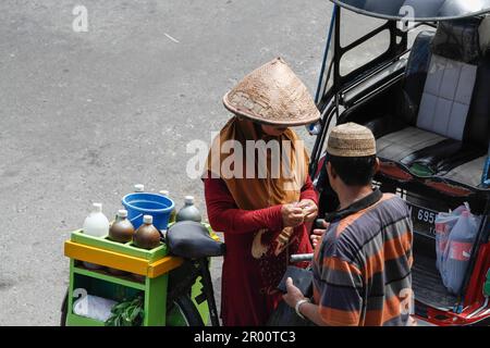 Kräutermedikamentenverkäufer und ihre Käufer. JAMU ist ein traditionelles Getränk in Indonesien, das aus verschiedenen Gewürzen und Pflanzen hergestellt wird. Stockfoto