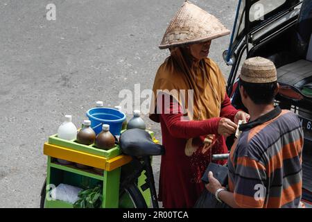 Kräutermedikamentenverkäufer und ihre Käufer. JAMU ist ein traditionelles Getränk in Indonesien, das aus verschiedenen Gewürzen und Pflanzen hergestellt wird. Stockfoto