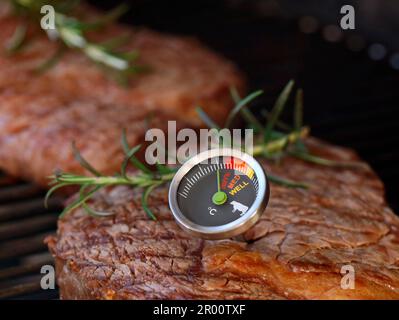 Köstliches Rindersteak auf dem Grillgitter mit einem Fleischthermometer, das eine Rarität von selten, mittel und gut zubereitet zeigt Stockfoto