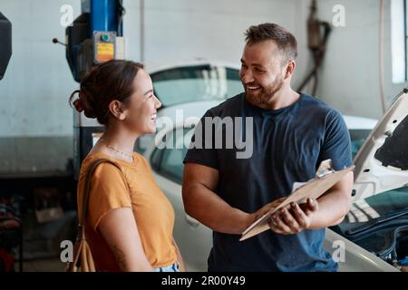 Wir haben alles repariert, was du erwähnt hast. Eine Frau, die mit einem Mechaniker in einer Autowerkstatt spricht. Stockfoto