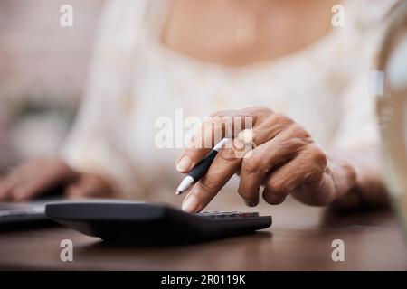 Sparen Sie Ihr Geld, retten Sie Ihr Leben. Eine nicht wiedererkennbare ältere Frau, die einen Taschenrechner benutzt, während sie ihre Finanzen zu Hause durchsucht. Stockfoto