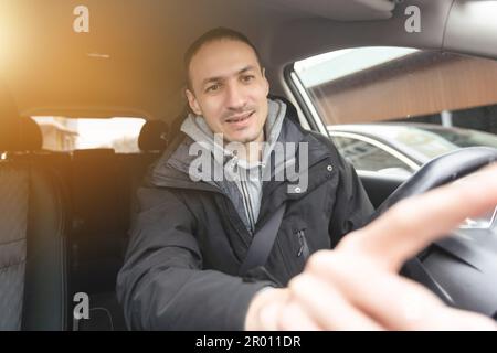 Hübscher junger Mann im Jeanshemd, der Touchscreen auf das Auto-Multimedia-Panel drückt und den wechselnden Radiosender umschaltet. Stockfoto