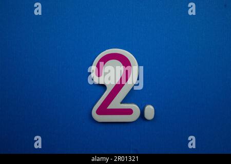 Die Zahl 2, pink und weiß, auf blauem Hintergrund, von oben fotografiert. Stockfoto
