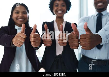 Positive Einstellung für den Sieg. Eine Gruppe von unbekannten Geschäftsleuten, die in einem Büro Daumen nach oben zeigen. Stockfoto