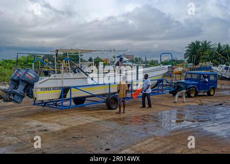 Die örtliche Besatzung bereitet sich darauf vor, ein leistungsstarkes Schnellboot mit einem Jeep-Fahrzeug von einem kleinen lokalen Hafen in Libreville aus auf eine Helling zu fahren. Stockfoto