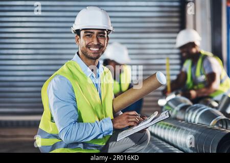 Ich bin der Beste für den Job. Ein attraktiver junger Bauunternehmer, der sich im Lagerhaus niederhockt und eine Bestandsaufnahme macht. Stockfoto