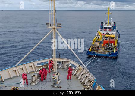 Die Besatzung eines seismischen Forschungsschiffs, das vor Bunkeroperationen das Abschleppseil von einem Offshore-Versorgungsschiff abschleppt. Stockfoto