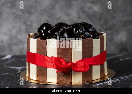 Kuchen mit Profiteroles und Schokoladencreme. Geburtstagskuchen oder Festtagskuchen. Kuchen mit Profiteroles und dunkler Schokoladencreme auf dunklem Hintergrund. Stockfoto