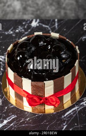 Kuchen mit Profiteroles und Schokoladencreme. Geburtstagskuchen oder Festtagskuchen. Kuchen mit Profiteroles und dunkler Schokoladencreme auf dunklem Hintergrund. Stockfoto