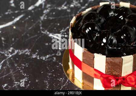 Kuchen mit Profiteroles und Schokoladencreme. Geburtstagskuchen oder Festtagskuchen. Kuchen mit Profiteroles und dunkler Schokoladencreme auf dunklem Hintergrund. Kopieren en Stockfoto