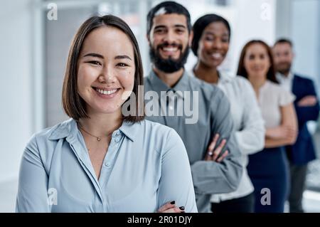 Große Dinge im Geschäftsleben werden immer von einem Team erreicht. Porträt einer Geschäftsfrau, die im Büro mit ihren Kollegen im Hintergrund steht. Stockfoto