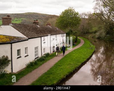 Blick von der Brücke über den Kanal auf den Mann und die Frau Fußweg vor einer schönen Reihe weiß getünchter Hütten an der Seite von Monmouthshire und Brecon Can Stockfoto