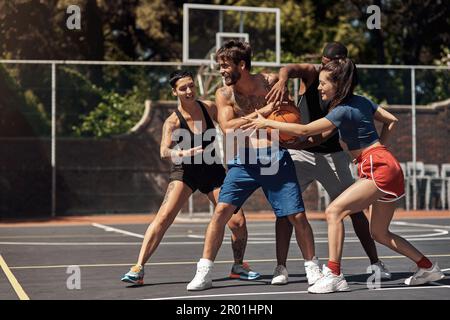 Beim Basketball dreht sich alles um schnelle Reaktionen. Eine Gruppe sportlicher junger Leute, die auf einem Sportplatz Basketball spielen. Stockfoto