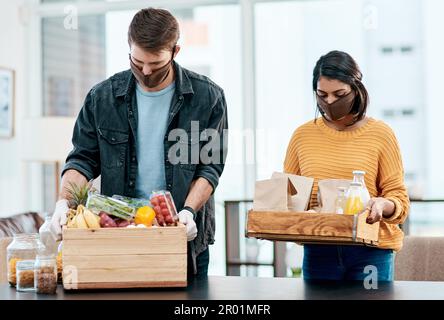 Machen Sie Ihre Sicherheit so wichtig wie Ihre Gesundheit. Ein junges Paar, das Masken trägt, während es zu Hause seine Lebensmittel auspackt. Stockfoto