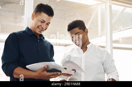 Das sieht toll aus. Zwei gutaussehende junge Geschäftsmänner, die sich ihre Notizen nach einem erfolgreichen Meeting im Vorstand ansehen. Stockfoto