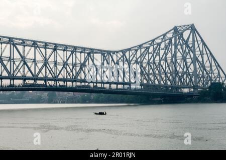 Ein Boot segelt auf dem heiligen Fluss Ganga mit dem Hintergrund der berühmten Howrah-Brücke im Norden von Kalkutta. Stockfoto