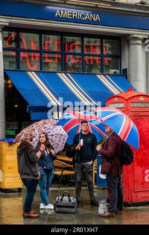 London, Großbritannien. 6. Mai 2023. Amerika trifft auf britische Tradition, als enttäuschte Royalisten versuchen, einen Ort zu finden, um Schutz zu suchen, nachdem sie von der Parade ausgeschlossen wurden - der Regen kam runter und Zehntausende Menschen waren enttäuscht und dazu verdammt, durch die Straßen zu wandern, als die Organisatoren die Tore sehr früh geschlossen hatten Morgen früh. Die Krönung von König Karl III. Am 6. Mai. Kredit: Guy Bell/Alamy Live News Stockfoto