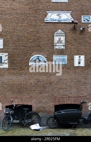 Alte Giebel an einer Wand, die Handwerke und Berufe der Hausbewohner mit Fahrrädern in Amsterdam, Holland, Niederlande, zeigen. Stockfoto