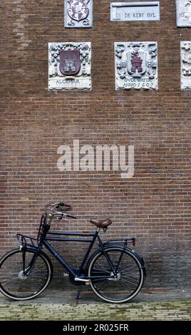 Alte Giebel an einer Wand, die Handwerke und Berufe der Hausbewohner mit Fahrrädern in Amsterdam, Holland, Niederlande, zeigen. Stockfoto