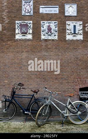 Alte Giebel an einer Wand, die Handwerke und Berufe der Hausbewohner mit Fahrrädern in Amsterdam, Holland, Niederlande, zeigen. Stockfoto