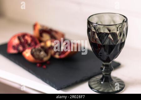 Granatapfel mit einem Glas Wein auf dem Tisch. Granatapfel mit Samen und Rotwein schneiden. Obst und Wein. Das Stillleben im Sommer. Alkoholische Getränke und reife Früchte. Stockfoto