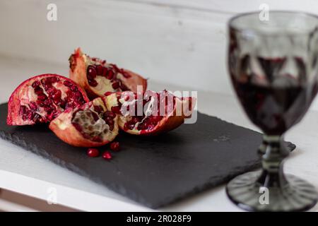 Granatapfel mit einem Glas Wein auf dem Tisch. Granatapfel mit Samen und Rotwein schneiden. Obst und Wein. Das Stillleben im Sommer. Alkoholische Getränke und reife Früchte. Stockfoto