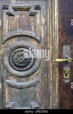 Schäbiger Teil einer alten Tür mit Dekorationen im Hintergrund. Teil einer Holztür mit Kratzern und einer alten abblätternden Farbe. Rustikale Vintage-Kulisse Stockfoto
